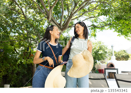 Laughing under sunny sky, two Asian women hold large straw hats by pool Laughing under sunny sky, two Asian women hold large straw hats by pool 135543341
