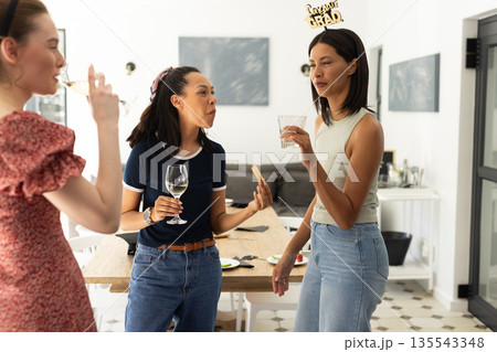 Laughing and chatting, three young women enjoy drinks at casual gathering Laughing and chatting, three young women enjoy drinks at casual gathering 135543348