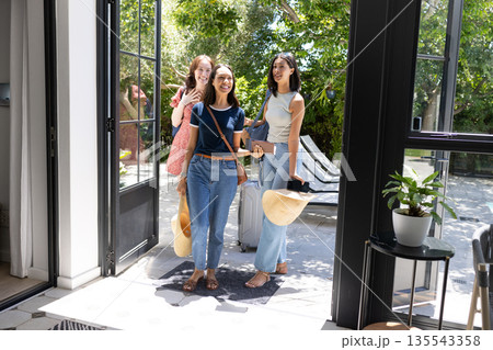 Entering sunlit garden, three young women smile warmly, holding straw hats Entering sunlit garden, three young women smile warmly, holding straw hats 135543358