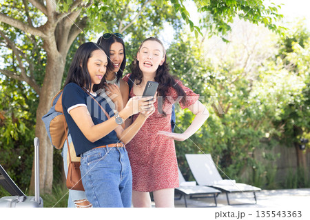 Three young women, one African American and two Caucasian, laughing while looking at smartphone outd Three young women, one African American and two Caucasian, laughing while looking at smartphone outd 135543363