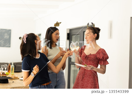 Celebrating indoors, three young women with diverse backgrounds clink glasses joyfully 135543399