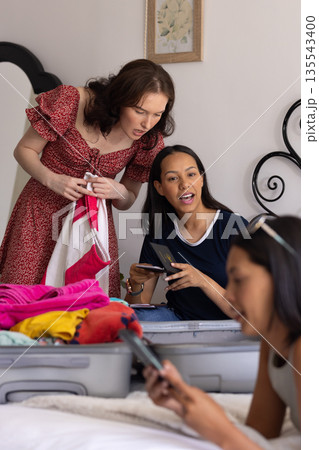 Packing colorful clothes into suitcase, three young women prepare for trip 135543400