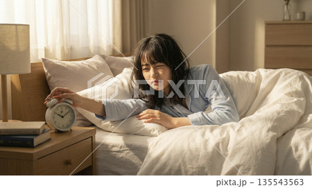 朝の光の中で目覚まし時計を止める寝起きの女子高生 眠い朝のルーティン 朝の光の中で目覚まし時計を止める寝起きの女子高生 眠い朝のルーティン 135543563