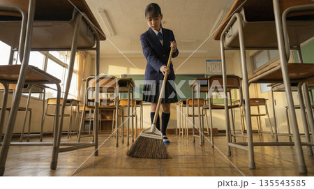 夕焼けの教室でほうきを使って床を掃く女子高生 放課後の掃除の時間 135543585