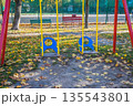 Children's swing on the playground. Yellow leaves in the playground. Gold autumn. Yellow leaves are scattered on the playground on a sunny day 135543801