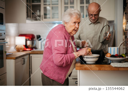 Elderly couple making dinner together in kitchen. Elderly couple making dinner together in kitchen. 135544062