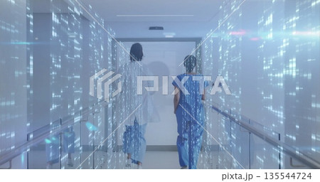 Two staff in scrubs and coat walking toward door in hospital corridor with holographic data streams 135544724