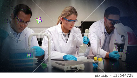 Female scientist wearing lab coat pipetting into microplate at bench, with multi-channel pipette 135544729