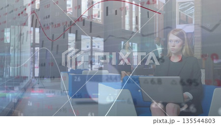 Woman in black blazer reviewing charts on silver laptop in office lobby, with blue sofas Woman in black blazer reviewing charts on silver laptop in office lobby, with blue sofas 135544803