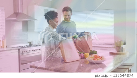 Unpacking couple placing green pepper on marble counter in bright modern kitchen with grocery bags 135544874