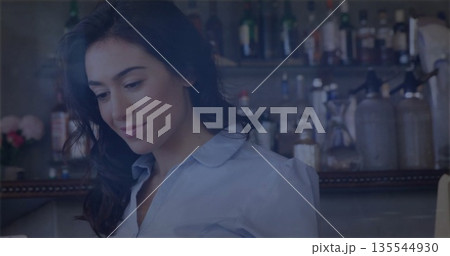 Smiling bartender arranging glassware at bar, with liquor bottles and pink flower vase, copy space 135544930