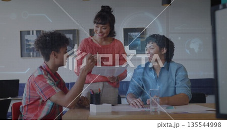 Three professionals collaborating around table in office, with printed documents pen and laptop 135544998
