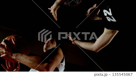 Jumping two male basketball players battling under hoop in sports hall, with basketball and jerseys Jumping two male basketball players battling under hoop in sports hall, with basketball and jerseys 135545067