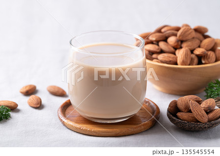 Glass of almond milk and almond nuts on white fabric background 135545554