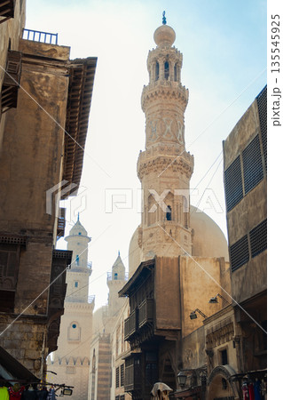 Historic Qalawun Complex in Cairo, featuring intricate architecture, tall minarets, and domes under a blue sky with clouds. A significant cultural landmark on Al-Muizz Street. Historic Qalawun Complex in Cairo, featuring intricate architecture, tall minarets, and domes under a blue sky with clouds. A significant cultural landmark on Al-Muizz Street. 135545925