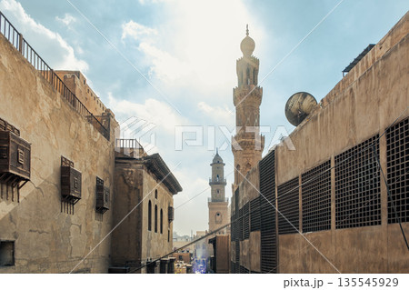 Historic Qalawun Complex in Cairo, featuring intricate architecture, tall minarets, and domes under a blue sky with clouds. A significant cultural landmark on Al-Muizz Street. 135545929