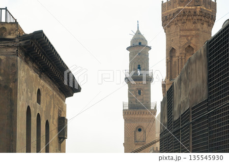 Historic Qalawun Complex in Cairo, featuring intricate architecture, tall minarets, and domes under a blue sky with clouds. A significant cultural landmark on Al-Muizz Street. 135545930