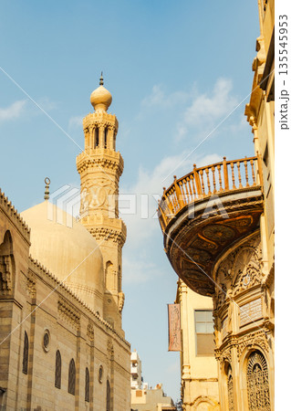 Historic Qalawun Complex in Cairo, featuring intricate architecture, tall minarets, and domes under a blue sky with clouds. A significant cultural landmark on Al-Muizz Street. 135545953
