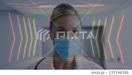 Standing doctor wearing surgical mask, lab coat, stethoscope in hospital corridor, with neon arrows 135546386