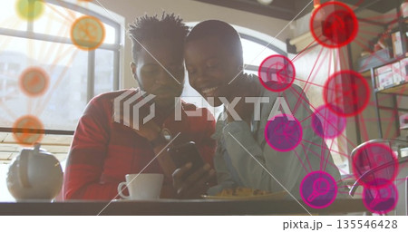Couple wearing red shirt and denim jacket checking smartphone at cafe, with digital network graphic 135546428