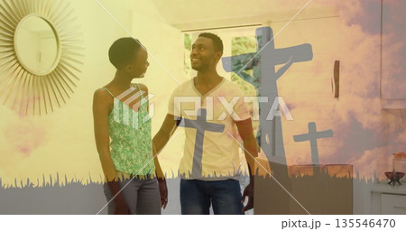 Standing couple wearing floral top and t-shirt in foyer, with sunburst mirror and cross overlay 135546470