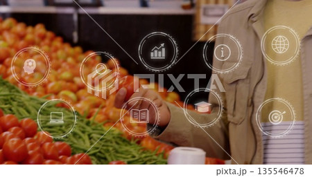 Selecting mid-adult man reaching for tomato at market with green beans, digital icons, copy space Selecting mid-adult man reaching for tomato at market with green beans, digital icons, copy space 135546478