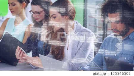 Working office colleagues analyzing data on laptop and documents in open office, with code overlay Working office colleagues analyzing data on laptop and documents in open office, with code overlay 135546505