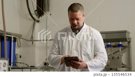 Inspecting equipment technician wearing lab coat using tablet in facility, with filter housings Inspecting equipment technician wearing lab coat using tablet in facility, with filter housings 135546534