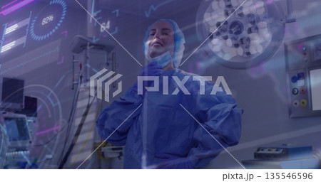 Standing female surgeon in scrubs monitoring data overlays in operating room, with anesthesia unit 135546596