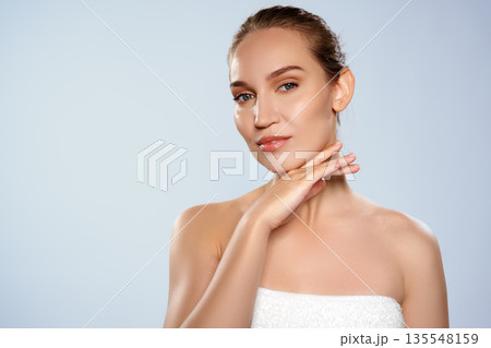 Woman poses with one hand on her chin against a light backdrop during a beauty shoot Woman poses with one hand on her chin against a light backdrop during a beauty shoot 135548159