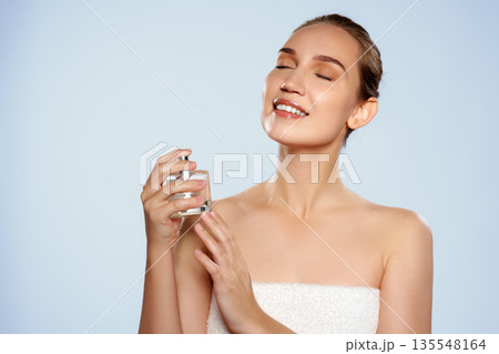 Woman holding a perfume bottle and enjoying a scent in a bright setting 135548164