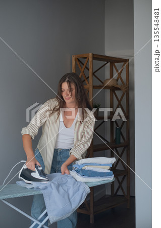 Home routine and quality clothing care with woman smoothing clothes with a steam iron for a neat organized wardrobe Home routine and quality clothing care with woman smoothing clothes with a steam iron for a neat organized wardrobe 135548481