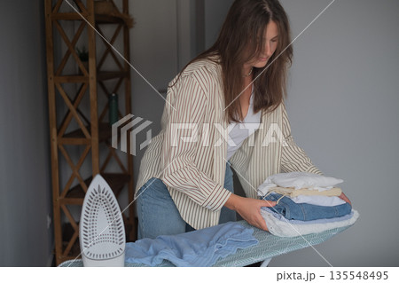 Home wardrobe care with woman smoothing clothes using a steam iron ensuring neatness and perfect garment appearance 135548495