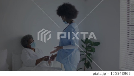 Holding patient hand, nurse in blue scrubs and mask standing at hospital bed, with stethoscope Holding patient hand, nurse in blue scrubs and mask standing at hospital bed, with stethoscope 135548965