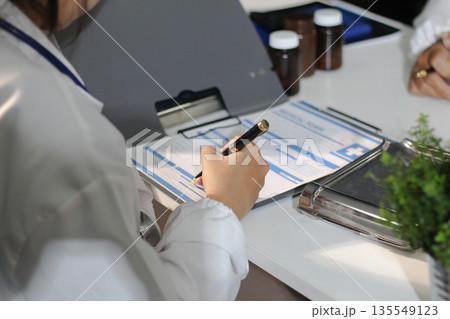 Medical team having a meeting with doctors in white lab coats and surgical scrubs seated at a table discussing a patients working online using computers in the medical industry. 135549123
