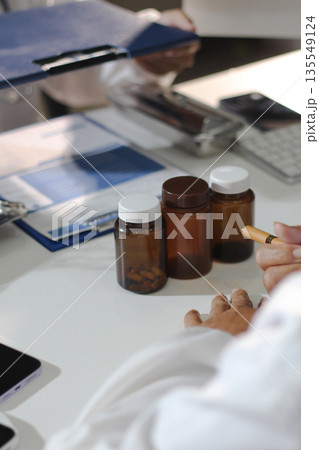 Medical team having a meeting with doctors in white lab coats and surgical scrubs seated at a table discussing a patients working online using computers in the medical industry. 135549124