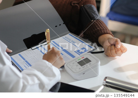 A doctor's hands carefully taking a patient's blood pressure using a sphygmomanometer. 135549144
