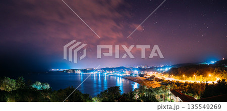 Mediterranean Bay Night Panorama – Illuminated Coastal Settlement with Palm Trees and Water 135549269
