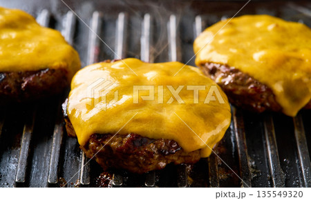 Beef burger patties sizzle and the cheese melts, on a grill. Beef burger patties sizzle and the cheese melts, on a grill. 135549320