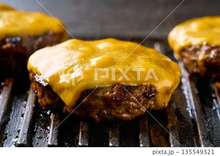 Melting cheese on a beef burger patties grilling a hot barbecue grill. 135549321