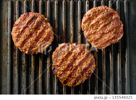 Beef burger meat patties grilling on a barbecue grill, top view. Beef burger meat patties grilling on a barbecue grill, top view. 135549325