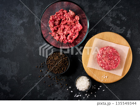 Raw burger beef patty on a black table, top view. Raw minced beef patty for burgers. Raw burger beef patty on a black table, top view. Raw minced beef patty for burgers. 135549344
