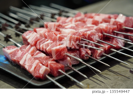 Raw, uncooked lamb skewers on a grill, a popular Chinese barbecue street food, ready for cooking. 135549447