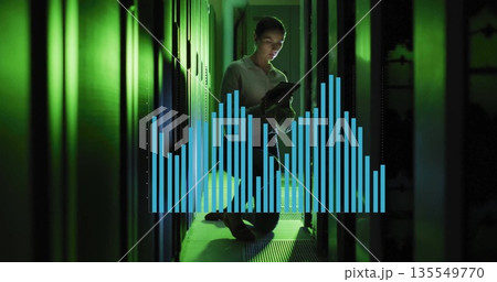 Kneeling technician holding tablet in narrow data center aisle, with floating bar-chart overlay 135549770