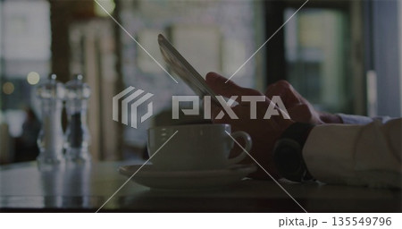 Tapping tablet, man in white shirt sitting at cafe table, with coffee cup and salt shakers 135549796