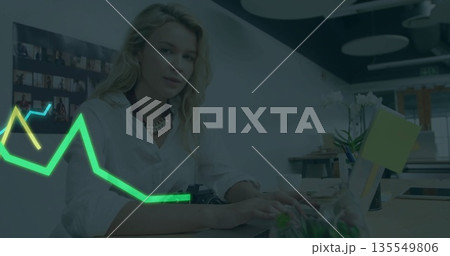 Typing professional wearing white shirt at office desk, with laptop, coffee mug, neon graph overlay 135549806