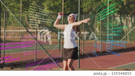 Serving female athlete tossing yellow ball on red hard court, with racket and code overlays 135549855