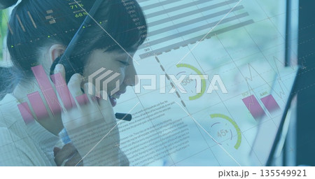 Speaking Asian agent wearing white collared top at office desk, with headset and data overlays Speaking Asian agent wearing white collared top at office desk, with headset and data overlays 135549921