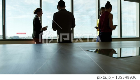 Office team in suits exchanging information using smart devices at conference table, with city view 135549936