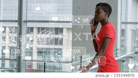 Talking woman in red dress holding smartphone by glass railing in office, overlay icons, copy space 135549970